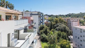 A modern apartment building with balconies, a rooftop garden, and a view of a hillside with trees.