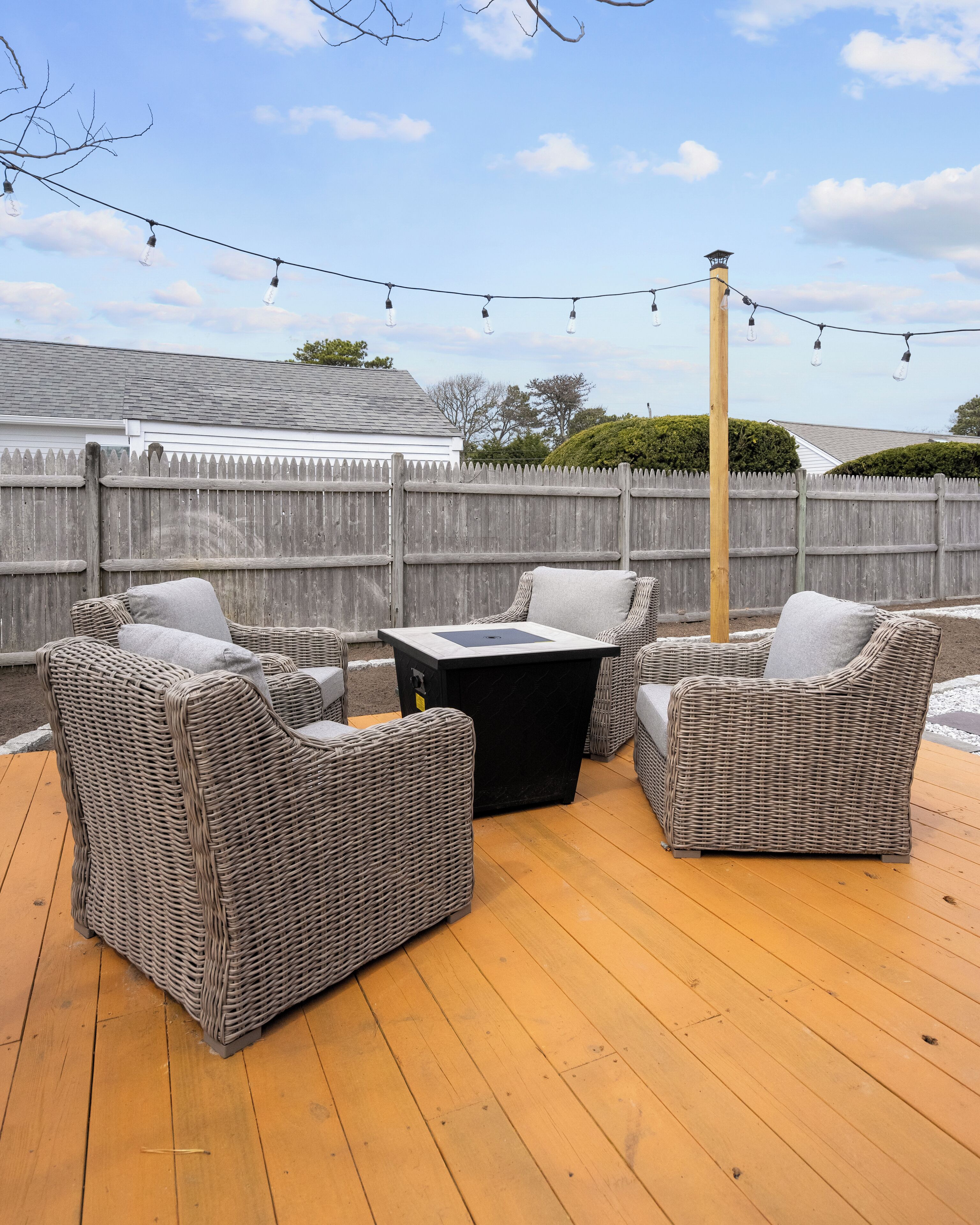 A deck with wicker furniture and a black table, surrounded by a wooden deck and a wooden fence.