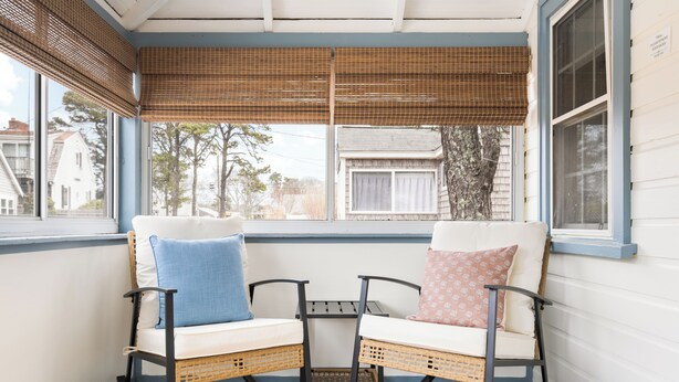 A covered porch with two rocking chairs, a small table, and a view of the neighborhood. - New! Beach Cottage - 3 min walk to Beach - Pet Friendly! (Dennis)
