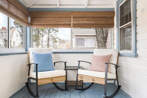 Eine überdachte Veranda mit zwei Schaukelstühlen, einem kleinen Tisch und Blick auf die Nachbarschaft.