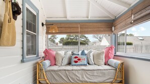 A cozy room with a wicker sofa, a wicker chair, and a window with a view of a white picket fence and trees. - New! Beach Cottage - 3 min walk to Beach - Pet Friendly! (Dennis)