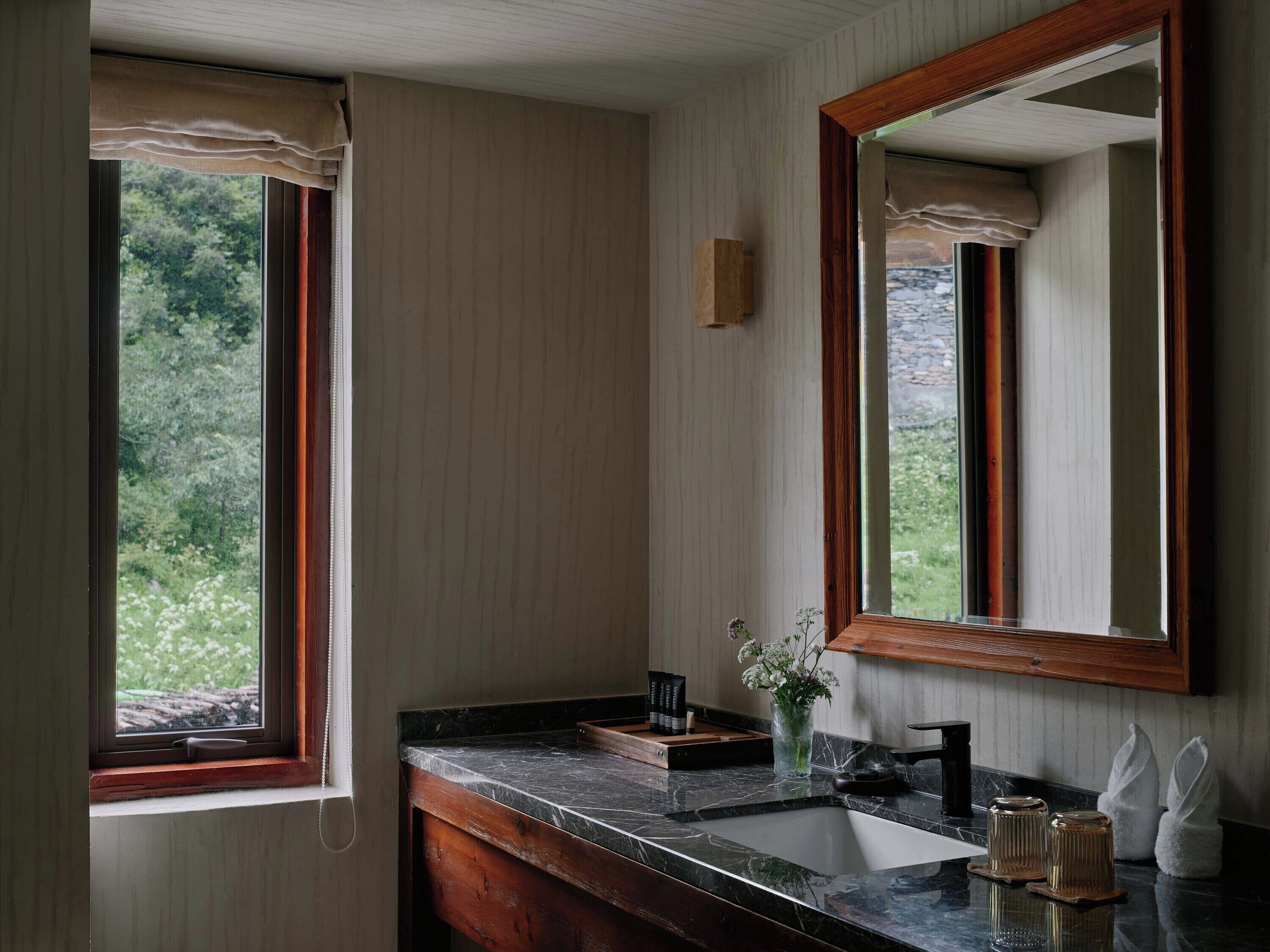 Un baño con lavamanos de mármol, tocador de madera y un espejo grande.