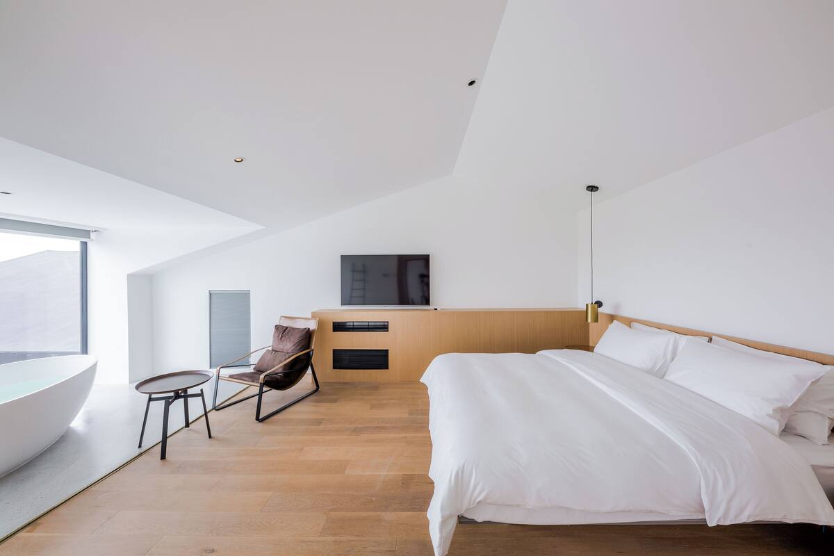Ein modernes Hotelzimmer mit einem großen Bett, einem Schreibtisch, einem Sessel und einem großen Fenster.