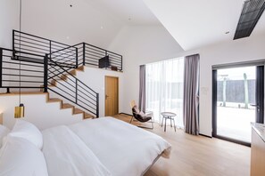 A modern bedroom with a large bed, a staircase with a black railing, a chair, and a small table. - The House Of Mo (Shanghai)