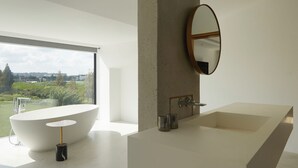 Une salle de bain moderne dotée d’une grande fenêtre, d’une baignoire sur pieds et d’un lavabo au design minimaliste.