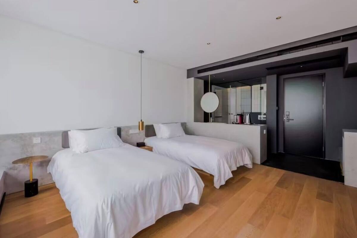 Ein modernes Hotelzimmer mit zwei Betten, einem großen Spiegel, einem runden Tisch und einer dunklen Tür.