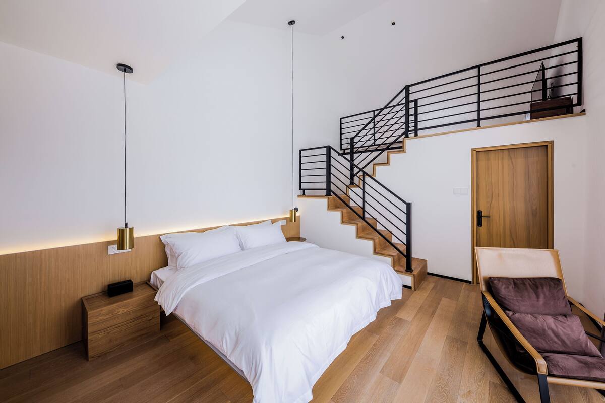 Ein modernes Schlafzimmer mit einem großen Bett, einem Nachttisch, einem Holzschrank, einem Stuhl und einer Treppe mit Geländer.