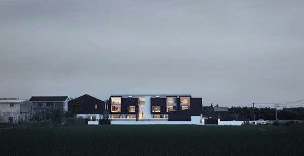 A modern multi-story house with large windows and a flat roof, surrounded by a grassy field and other buildings. - The House Of Mo (Shanghai)