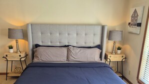 Een slaapkamer met een groot bed, twee nachtkastjes met lampen, een plafondventilator en een raam met zonwering.