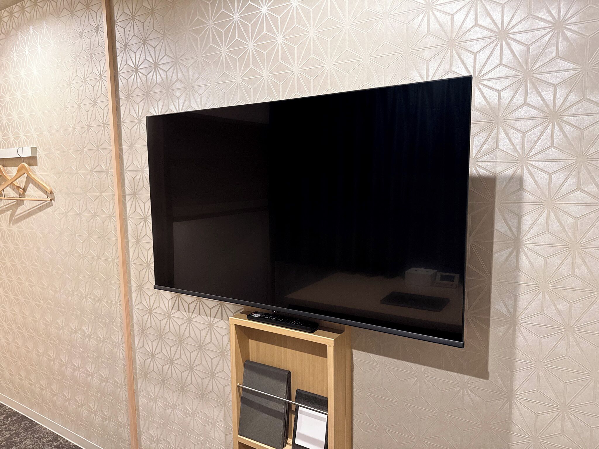 A flat-screen TV mounted on a wall with a geometric patterned wallpaper.