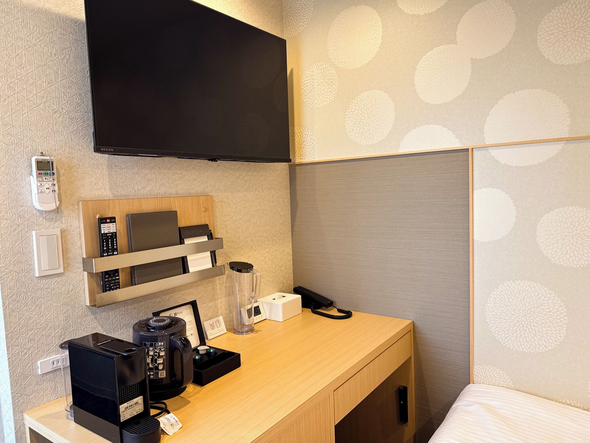Une chambre d’hôtel avec un bureau en bois, une machine à café, un téléphone et un téléviseur fixé au mur.