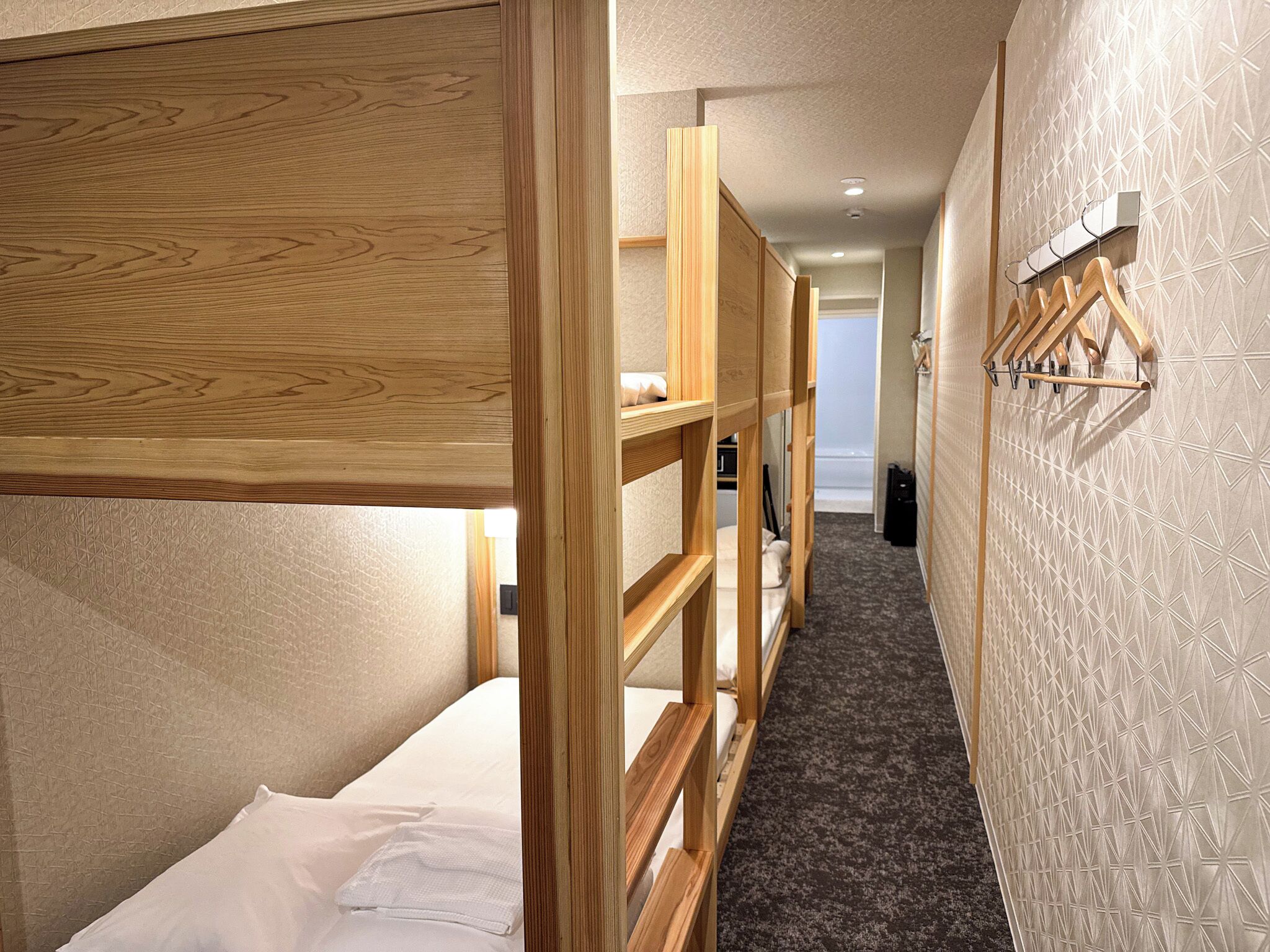 A narrow hallway with bunk beds on either side, a wooden bench in the center, and a wall-mounted rack with hangers.