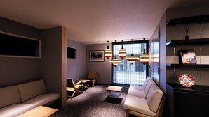 Ein modernes Hotelzimmer mit einer Couch, Sesseln, einem kleinen Tisch und einer dekorativen Platte in einem Schrank.