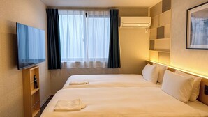 Ein Hotelzimmer mit zwei Betten, einem Flachbildfernseher, einer Klimaanlage und einem großen Fenster mit Vorhängen.