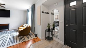 A modern living room with a sofa, a rug, a small table with plants, a mirror, and a black door.