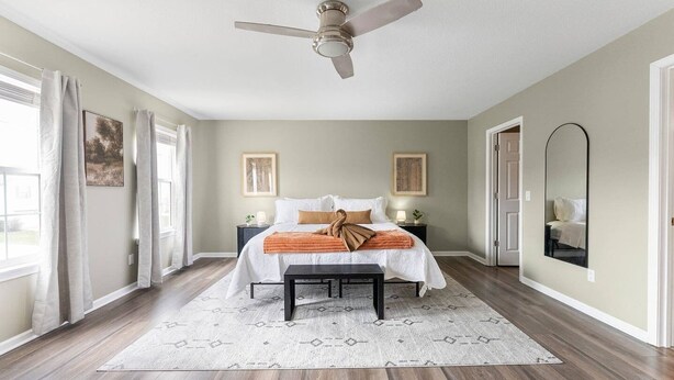A bedroom with a bed, bedside tables, a ceiling fan, a large mirror, and a window with curtains.