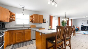 A kitchen with wooden cabinets, a central island, a dining area with chairs, and a living room with a sofa and a TV.