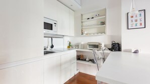 A modern kitchen with white cabinetry, a microwave, a toaster, and a hanging light fixture.