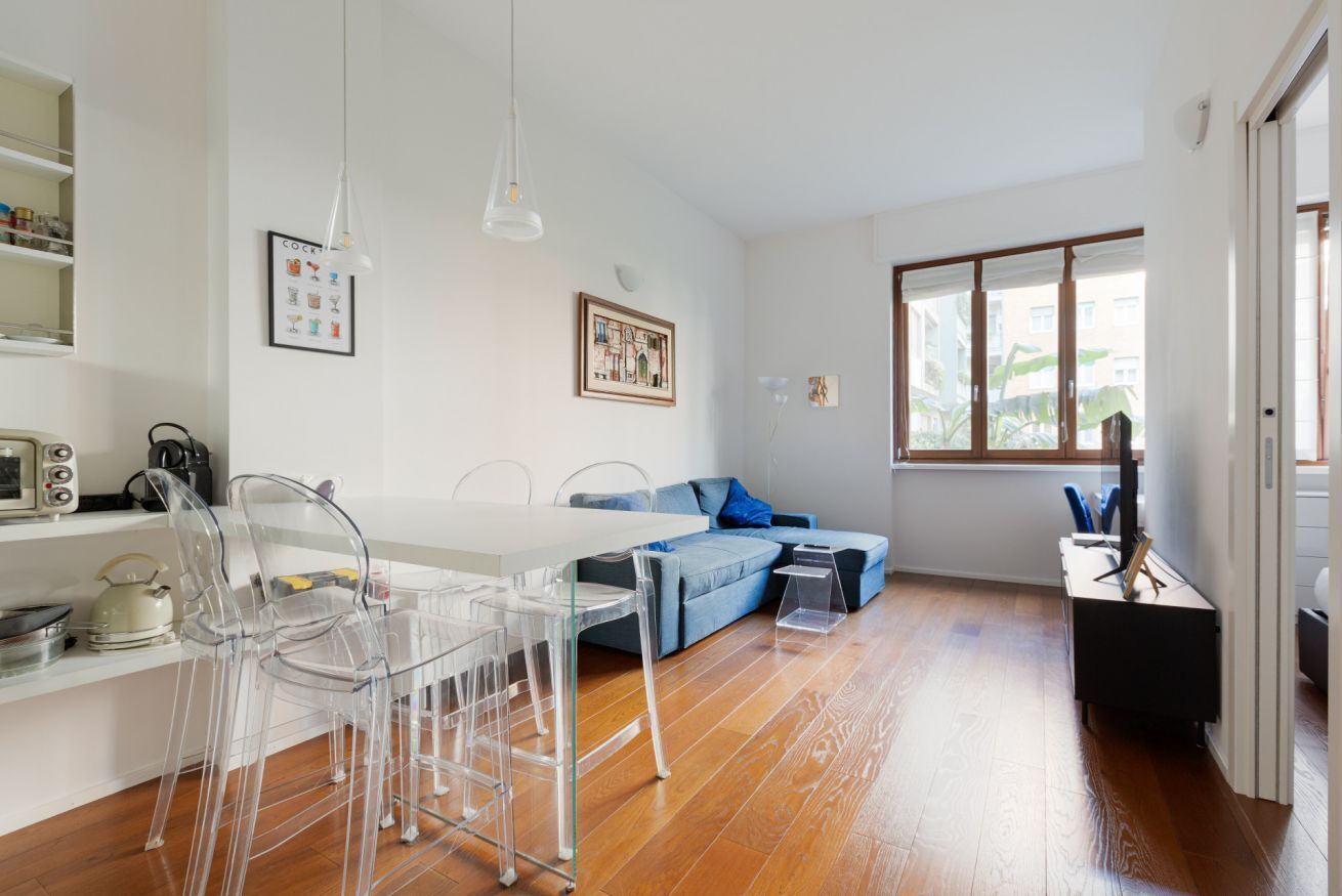 A modern living room with a dining table, chairs, a sofa, and a television.