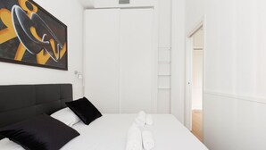 A hotel room with a bed, black and white pillows, a painting on the wall, and a white door.