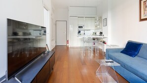A modern living room with a flat-screen TV, a blue sofa, and a glass coffee table.