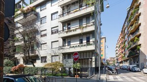 A multi-story building with balconies, a stop sign, and parked vehicles.