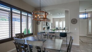 A dining area with a wooden table and chairs, a chandelier, and a view through large windows. - Luxury 3 bedroom in gated Grayhawk community (Scottsdale)