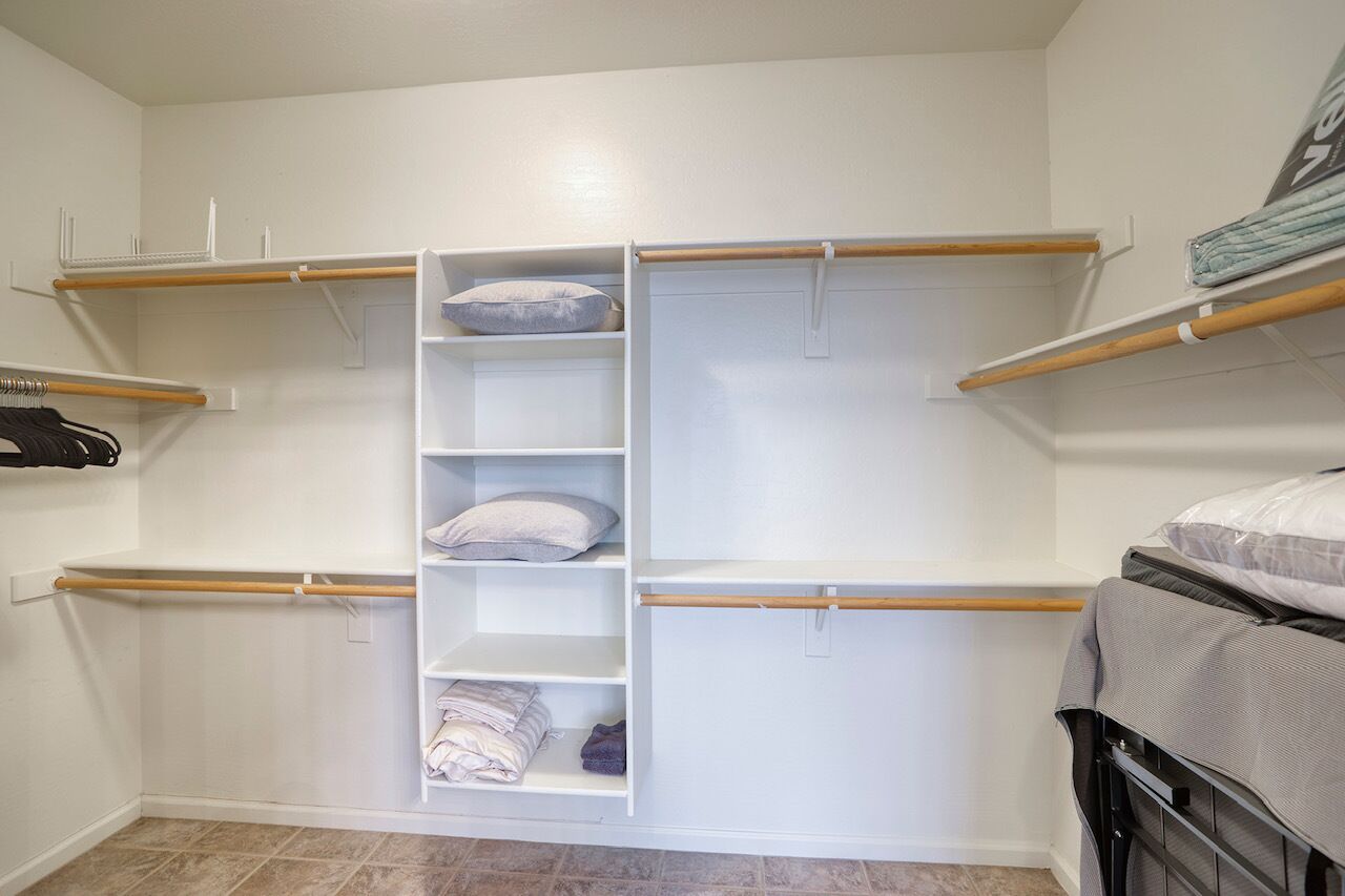 A walk-in closet with open shelving, a hanging rod, and a bed with a gray blanket.