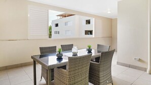 Un comedor con una mesa, sillas, ventilador de techo y vista a un edificio a través de una ventana.