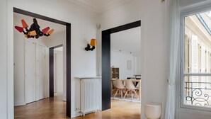 A spacious hallway with wooden flooring, white walls, and a view of a dining area with chairs and a table.