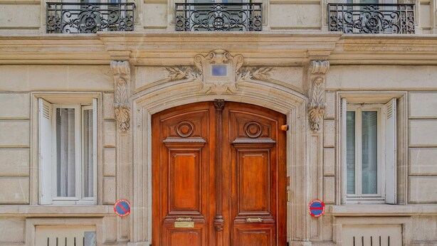 A double wooden door with ornate carvings and a balcony above.