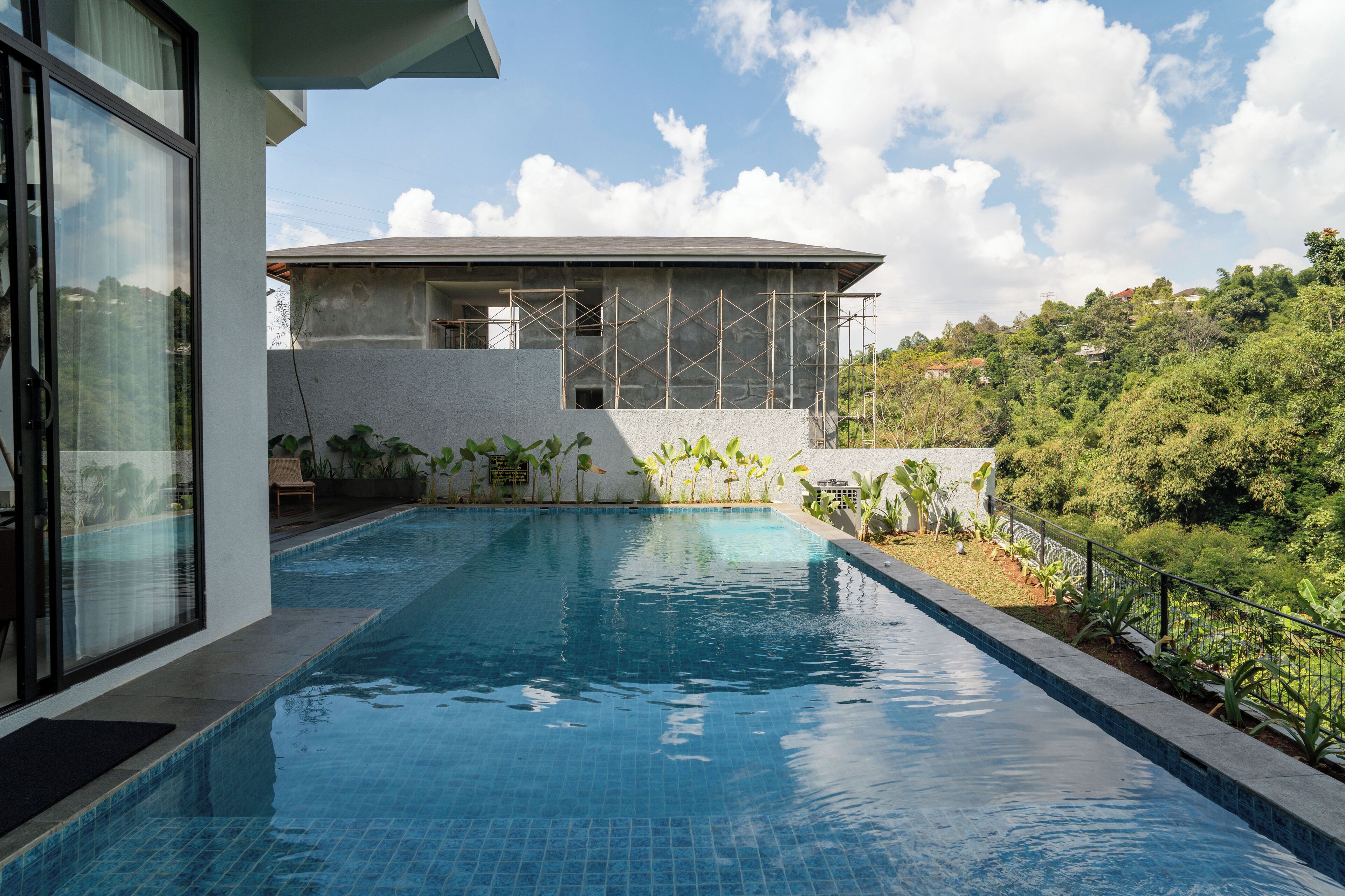 Piscina con vista a un edificio en construcción y follaje circundante.