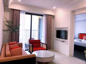 Ett modernt hotellrum med en soffa, ett runt bord, en TV och en balkong med gardiner.