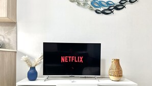 Un televisor de pantalla plana sobre un mueble blanco con un jarrón y un objeto decorativo en la pared de fondo.