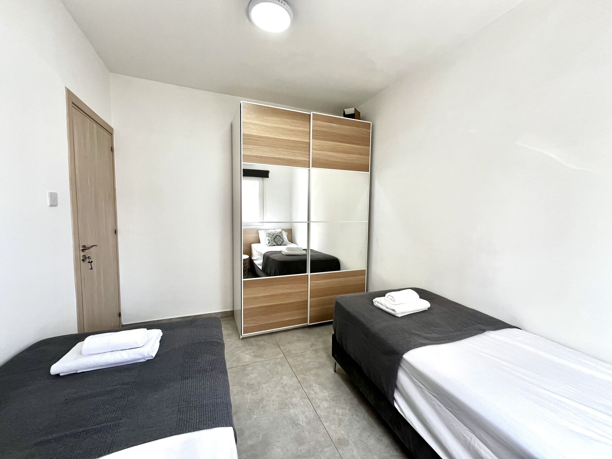 Une petite chambre moderne avec deux lits simples, une armoire en bois et un miroir.