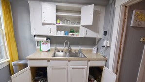 A compact kitchen with white cabinets, a stainless steel sink, and a countertop with various kitchen items.