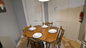 A dining room with a wooden table set for four, chairs, a white door with a no smoking sign, and a fire extinguisher mounted on the wall.