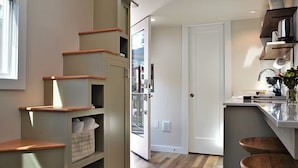 Une cuisine moderne dotée d’une cuisinière intégrée, d’étagères en bois et d’une porte blanche donnant sur une autre pièce.
