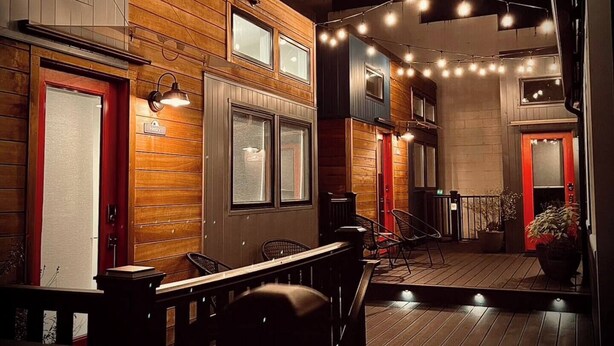Un espace intérieur accueillant et bien éclairé, avec des murs en bois et une terrasse en bois. On y trouve plusieurs coins salon avec des chaises et des tables, et un panneau indiquant un « hôtel » sur le côté gauche.