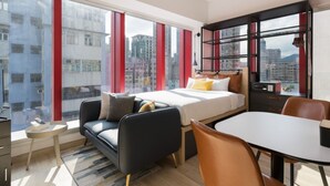 Un hotel moderno con una cama grande, un sofá, una mesa de comedor y vistas a la ciudad a través de amplias ventanas.