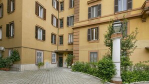 A multi-story building with a yellow facade, multiple windows with shutters, and a central entrance. - Family stay in Trastevere (Rome)