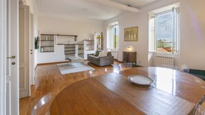 A spacious living area with a wooden dining table, a sofa, and a view of the city through large windows. - Family stay in Trastevere (Rome)