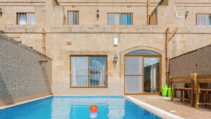 A swimming pool with a wooden deck and benches, surrounded by stone walls and windows. - Ta Dora Sleeps 6 with Private Pool (Xaghra)