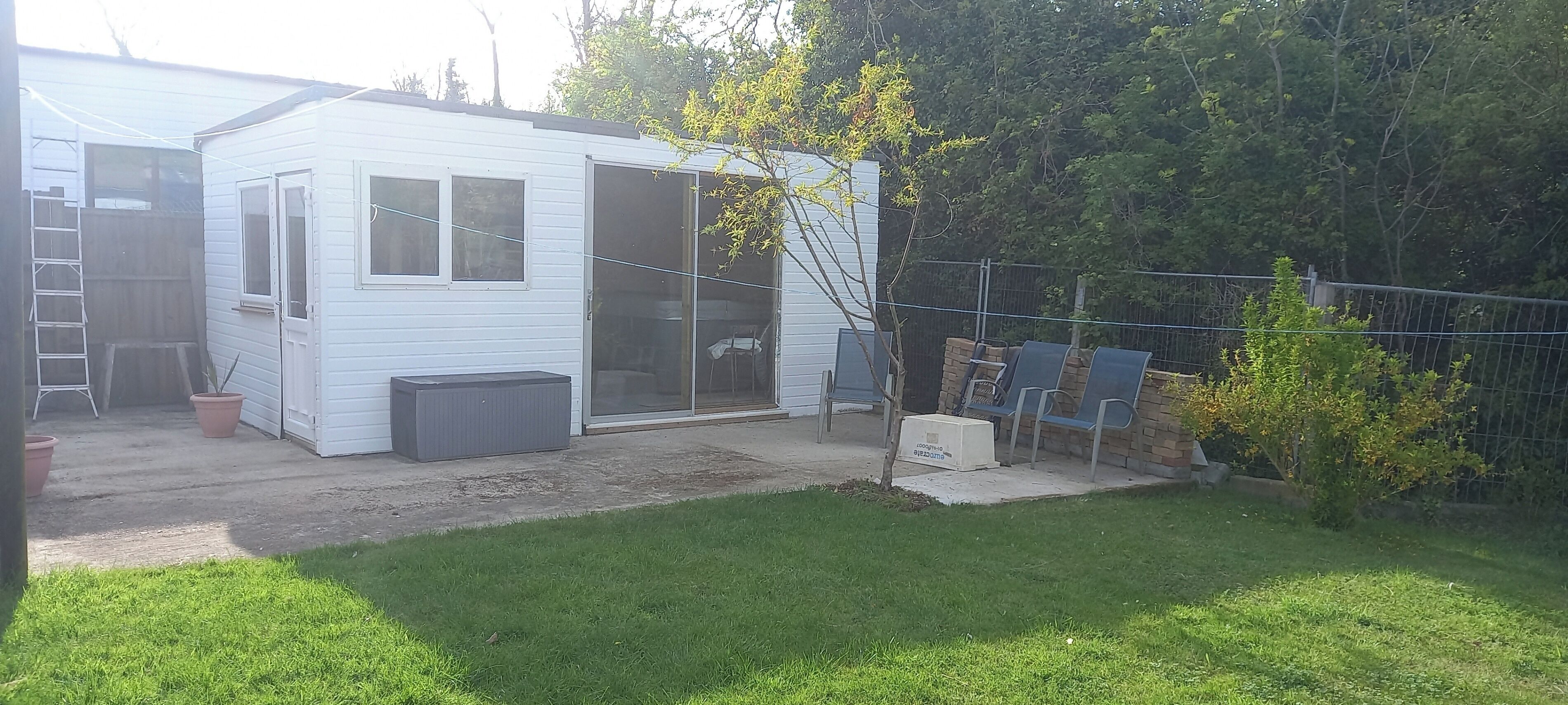 A small white house with a sliding glass door, a concrete patio, and a fenced backyard with a lawn.