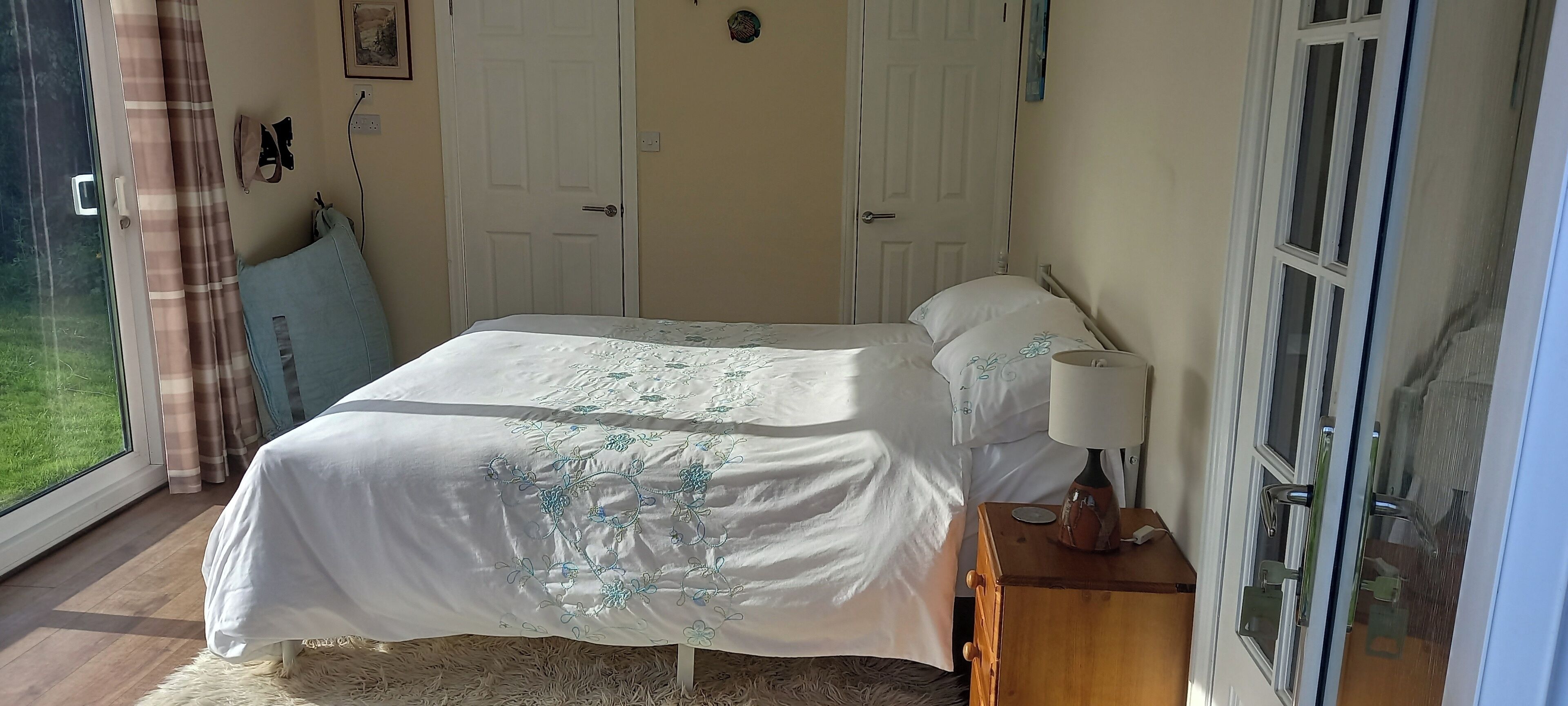 Une chambre à coucher avec un lit, une table de chevet, une lampe et une fenêtre avec des rideaux.