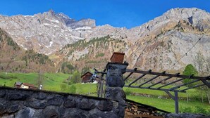 Eine Berglandschaft mit einer Steinmauer, einer Holzpergola und einem Haus im Tal.