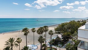 A beach view with palm trees, a pool, and a building with balconies. - Estepona Beachfront Promenade by Libehomes (Estepona)