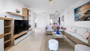 A modern living room with a flat-screen TV, wooden shelving, a sofa, a coffee table, and a painting of a sunset over the ocean. - Estepona Beachfront Promenade by Libehomes (Estepona)