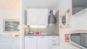 A compact kitchen with white cabinets, a built-in microwave, and a painting of a seascape. - Rena Bianca Mono - 5 mins from the beach, WiFi, AC (Olbia)