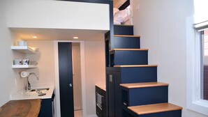 A compact kitchen with a wooden table, built-in cabinets, and a staircase with wooden steps.